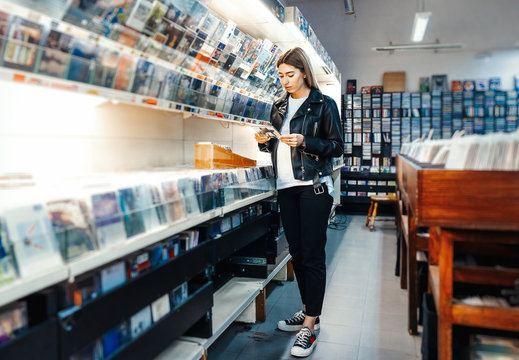 Young attractive woman choosing vinyl record in music record shop.