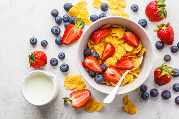 Cornflakes with strawberries and blueberries in a bowl on white background, top view.