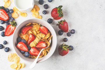 Cornflakes with strawberries and blueberries in a bowl on white background, top view.