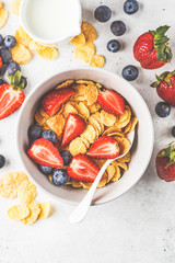 Cornflakes with strawberries and blueberries in a bowl on white background, top view.