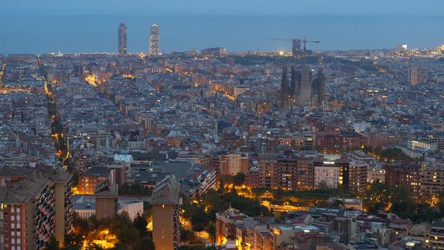 Barcelona panorama from viewpoint at top of hill, shoot at blue hour. Time lapse view of cityscape at nightfall, warm lights on streets, many buildings spread around flat landscape
