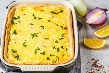Onion pie with cheese and herbs in black baking dish.