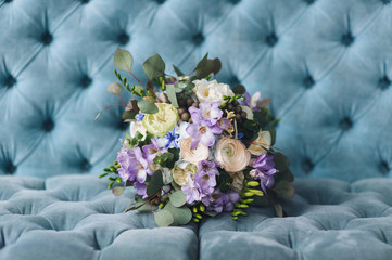 A beautiful multicolored wedding bouquet with wildflowers and roses lies against the blue sofa. Wedding photography, copy space, poster.