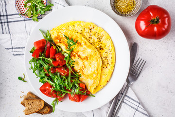 Classic omelet with cheese and tomatoes salad on white plate, top view.