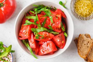 Tomatoes and arugula salad with sprouts and olive oil in gray bowl, top view.