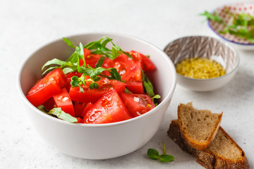 Tomatoes and arugula salad with sprouts and olive oil in gray bowl.