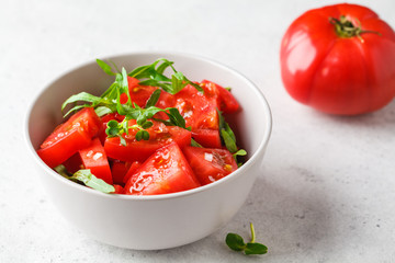Tomatoes and arugula salad with sprouts and olive oil in gray bowl.