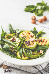 Grilled zucchini salad with arugula and nuts in white plate. Healthy vegan food concept.