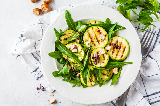 Grilled zucchini salad with arugula and nuts in white plate. Healthy vegan food concept.