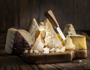 Piece of Parmesan cheese  on the wooden board. Assortment of different cheeses at the background.