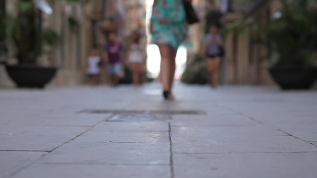 Woman wearing flat shoes walk at old stony pavement of Barceloneta street, low camera, blurred background. Lady come towards, appear from bokeh and pass by