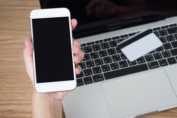 People are using smartphones to pay via a credit card placed on a laptop on a wooden table. Black screen.