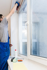 Close-up of a man in uniform and blue gloves washes a windows with window scraper. Professional home cleaning service