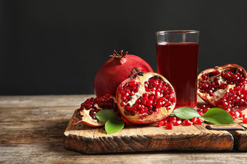 Glass of pomegranate juice and fresh fruits on wooden board against black background, space for text - obrazy, fototapety, plakaty