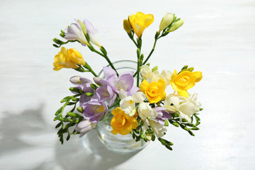 Bouquet of fresh freesia flowers in vase on table, above view