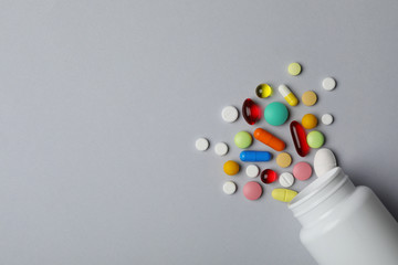 Bottle with different pills on grey background, flat lay. Space for text