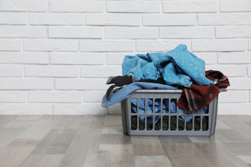 Laundry basket with dirty clothes on floor near brick wall. Space for text