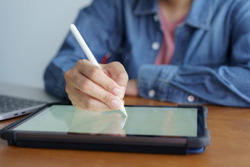 Close up hand working woman work and writing on tablet. On wooden desk background have laptop.