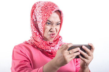 Portrait of Asian muslim lady wearing hijab with funny face playing games on tablet