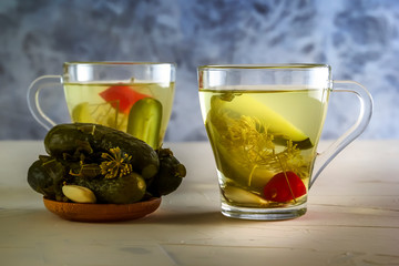 Two glasses with cucumber pickle and pickled cucumbers in a wooden plate. Close-up