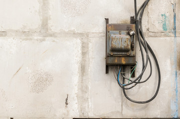old rusty unkempt electric shield with a switch on the wall of an industrial building made of concrete blocks with molten wires sticking out of it - Powered by Adobe