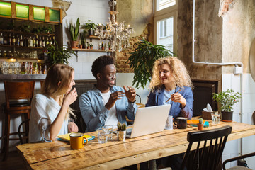 Multiracial group of three friends having a coffee together. Serious focused african man and two women at cafe, talking, laughing and enjoying their time. Lifestyle,friendship concept with real people