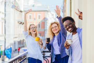 Group of three multiethnic business people friends coworkers chatting meeting, drinking coffee, sharing positive emotions on balcony in sunny morning.