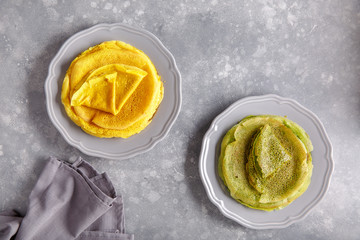 Yellow and green pancakes on gray plate.  Stack of spinach crepes and crepes tinted turmeric on concrete background. Top view, copy space.