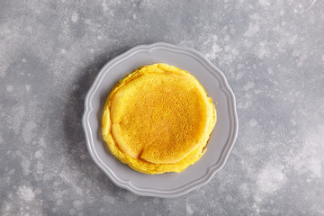 Yellow pancakes on gray plate.  Stack of crepes tinted turmeric on concrete background. Top view, copy space.