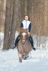 A young woman riding a brown horse in the winter forest