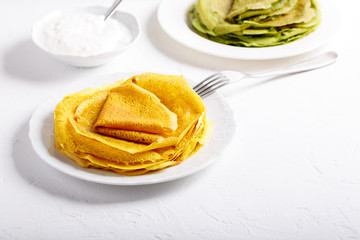 Yellow and green pancakes on white plate.  Stack of spinach crepes and crepes tinted turmeric on white background.