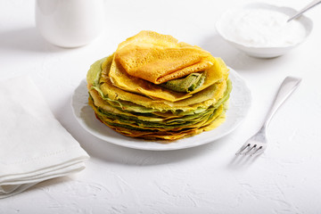 Yellow and green pancakes on white plate.  Stack of spinach crepes and crepes tinted turmeric on white background.