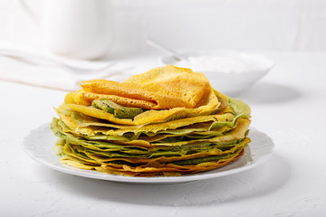 Yellow and green pancakes on white plate.  Stack of spinach crepes and crepes tinted turmeric on white background.