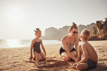 Smiling Mother playing with her laughing children on a beach