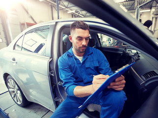 car service, repair, maintenance and people concept - auto mechanic man or smith with clipboard writing at workshop