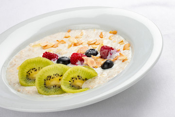 Oatmeal breakfast with berries and kiwi on white background