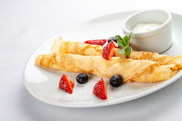 Wheat pancakes with berries and sour cream on white background