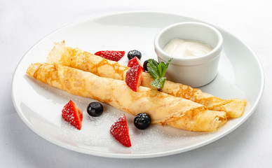 Wheat pancakes with berries and sour cream on white background