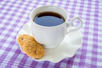 White porcelain saucer with wavy edge and cup of tea and sweet cookies on it. Oat cookies with pieces of dark chocolate. Sweet high-calorie breakfast.