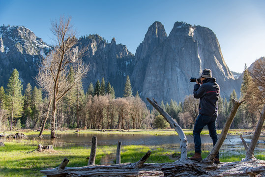 Asian man photographer and tourist holding DSLR camera taking photo of Cathedral Rock landscape in Yosemite National Park, famous natural attraction in California, USA. Travel photography concept