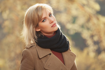 Young fashion woman in beige coat walking in autumn park