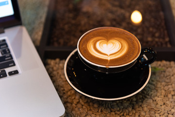 A cup of latte art coffee with laptop computer on table with coffee beans backgrounds