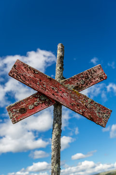 Closeup of a red old worn wooden footpath trail sign. Outdoor Cross against blue sky.