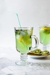 Refreshing lemonade from kiwi and lemon with ice on a light background. Vertical orientation