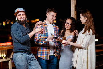 friends with smiles on their faces in the bar have fun, drink cocktails, clink glasses.