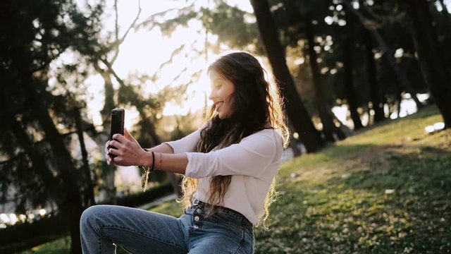 Young pretty woman taking selfie with smartphone in a green park