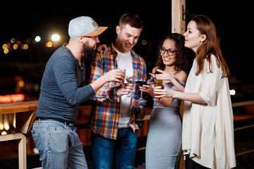 friends with smiles on their faces in the bar have fun, drink cocktails, clink glasses.