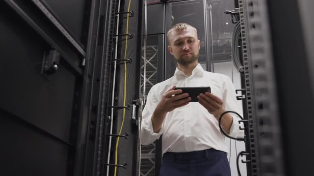 Man opening server rack of hosting system in big data center for support software using phone. IT engineer controlling routers and do diagnostics for search problems in cloud security technology