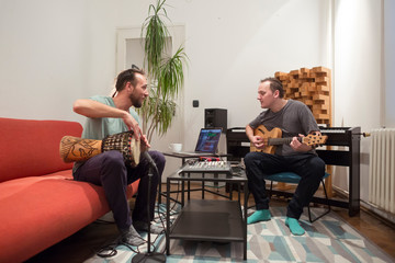 Two musicians playing instruments in home music studio.