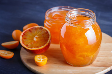 Orange and kumquat jam in a glass jar with fresh fruits on a wooden kitchen board.